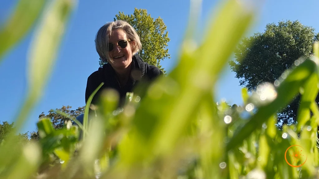 eine Frau steht hinter Gräsern und lächelt in die Kamera.