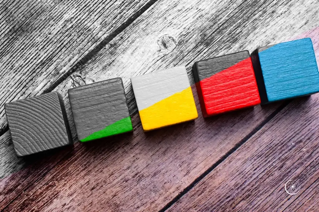 Depression braucht bunt - Eine Reihe Holzbauklötze in grün, gelb, rot und blau auf einer Holzunterlage