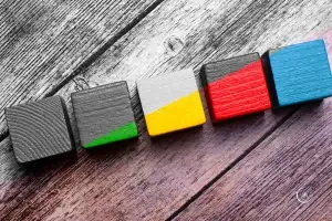 Depression braucht bunt - Eine Reihe Holzbauklötze in grün, gelb, rot und blau auf einer Holzunterlage