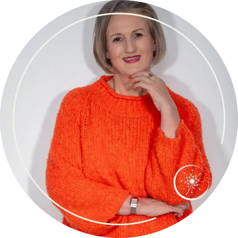 Stefanie Koch steht im orangefarbenen Pullover vor einer hellen Wand. Bild als Halbportrait aufgenommen.