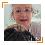 Frau mit Brille und wilder Frisur schaut zusammen mit einem Mops in die Kamera - Nahaufnahme