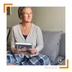 Frau sitz in bequemer Kleidung auf einer Couch, hat ein Notzbuch in der Hand und schaut nach rechts