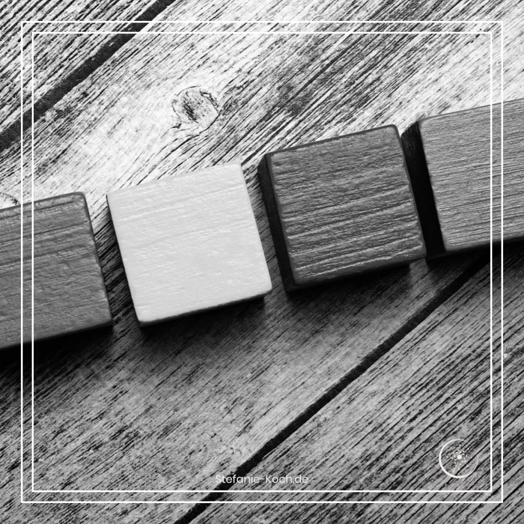 Eine Reihe von vier Bauklötzen auf einer Holzunterlagen - alles ist schwarz-weiß.