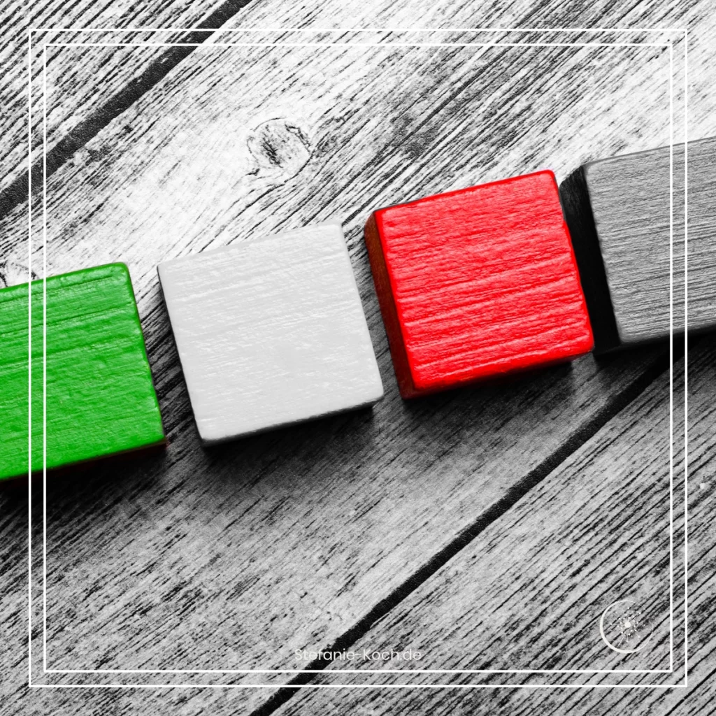 Eine Reihe von vier Bauklötzen auf einer Holzunterlagen - alles ist schwarz-weiß. Ein Bauklotz leuchtet rot, ein anderer grün.