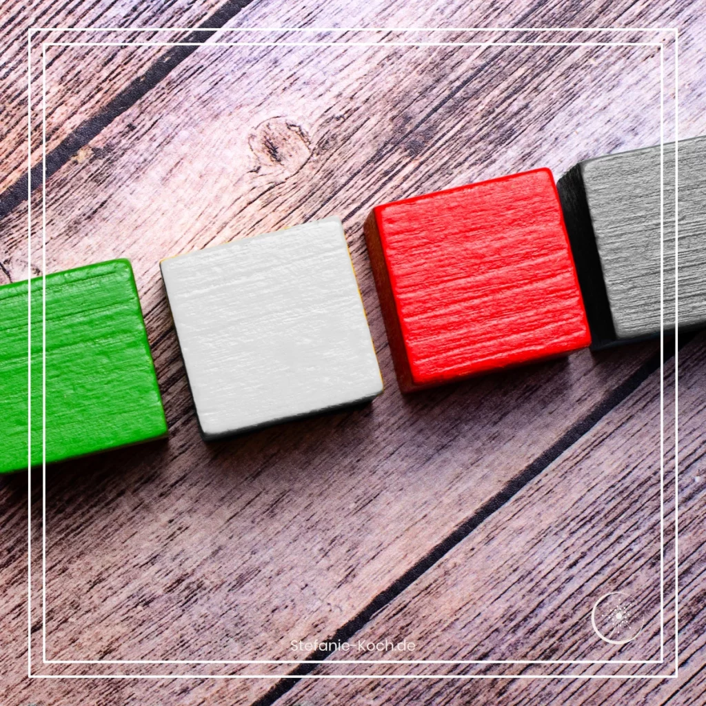 Eine Reihe von vier Bauklötzen auf einer Holzunterlagen - alles ist schwarz-weiß. Ein Bauklotz leuchtet rot, ein anderer grün. Die Unterlage ist holzfarbend.