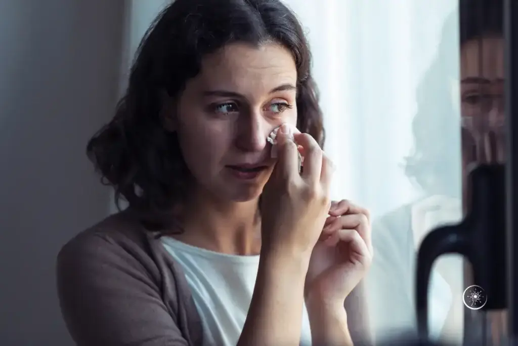 Depression Sinn finden - Eine Frau Anfang 40 steht vor einem FEnster und wischt sich mit einem Taschentuch eine Träne weg