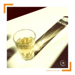 Ein Glas steht im Sonnenstrahl und wirft einen leuchtenden Schatten.