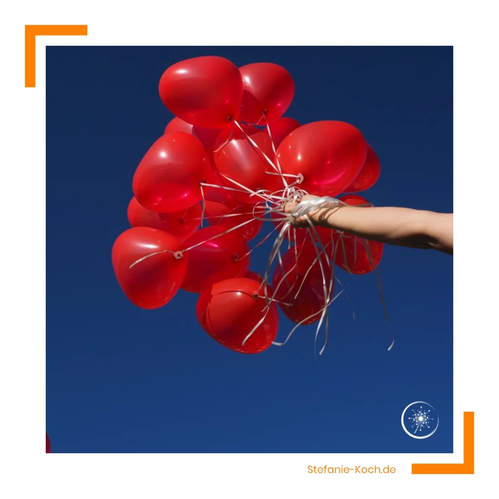 eine Hand hält viele roten Luftballons in einen strahlend blauen Himmel