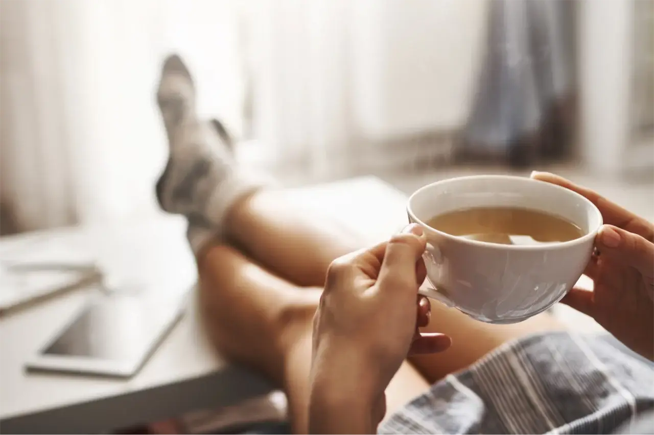 Dein Jahresmotto in 9 Schritten - Frauenbeine liegen gemütlich auf einem Tisch, in den Händen ist eine Teetasse