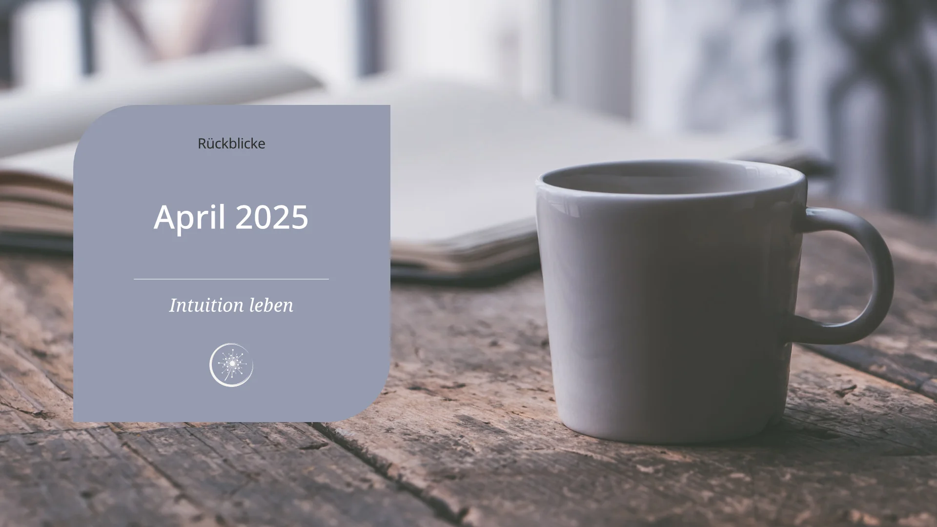 April 2025 - eine graue Keramiktassse steht auf einem alten Holztisch. Im Hintergrund liegt ein offenes Buch