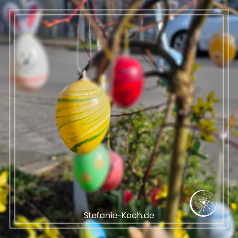 Bunte Kunststoffostereier an einem Strauch am Straßenrand.