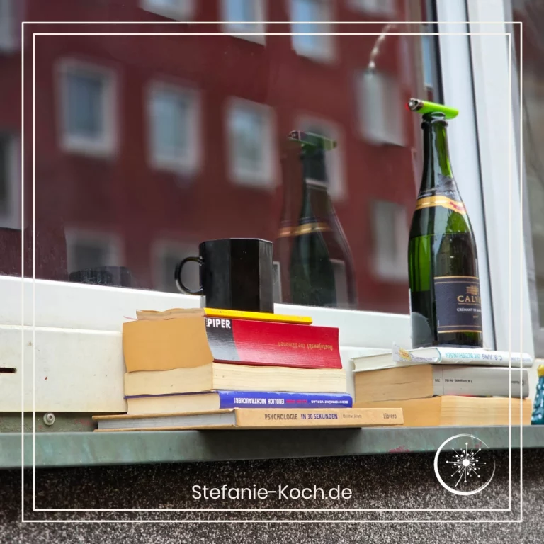 Bücher, eine Kaffeetasse und eine Sektflasche stehen draußen auf einer Fensterbank.