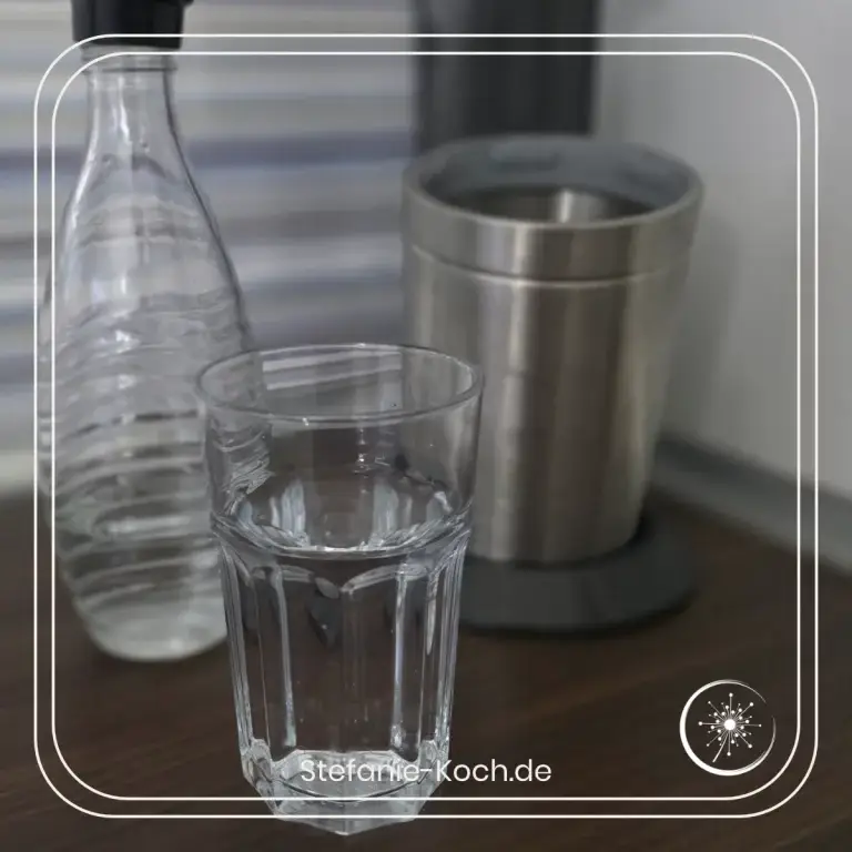Ein Glas Wasser, eine Glasflasche und einSpdastream in einer Küchenecke.