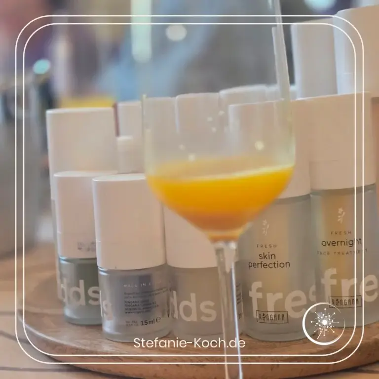 Ein Glas Orangensekt mit Kosmetikflakons im Hintergrund