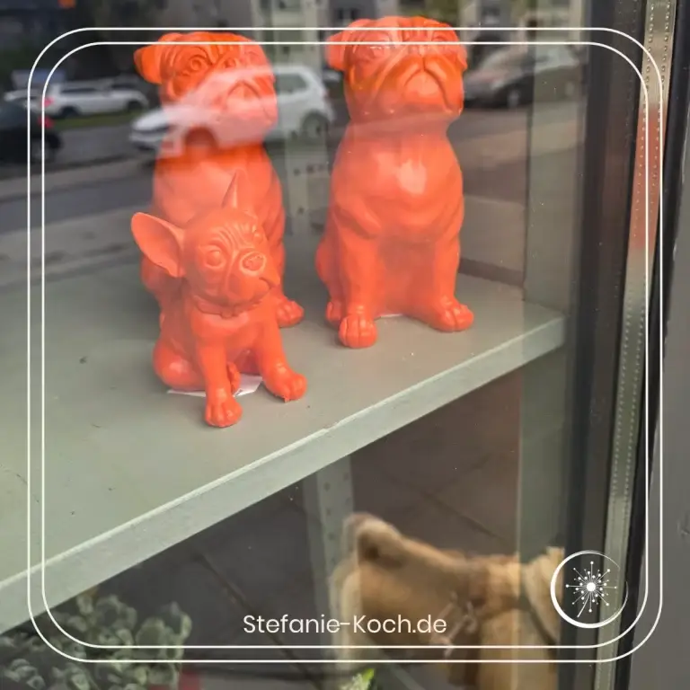 Blick in ein Schufenster mit den 2 Mopsfiguren und einer Frenchbulldog-Figur in Orange.