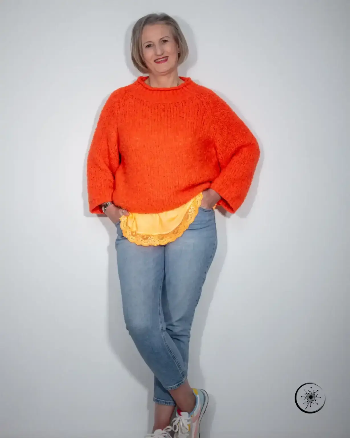 Stefanie Koch steht im orangefarbenen Pullover vor einer hellen Wand