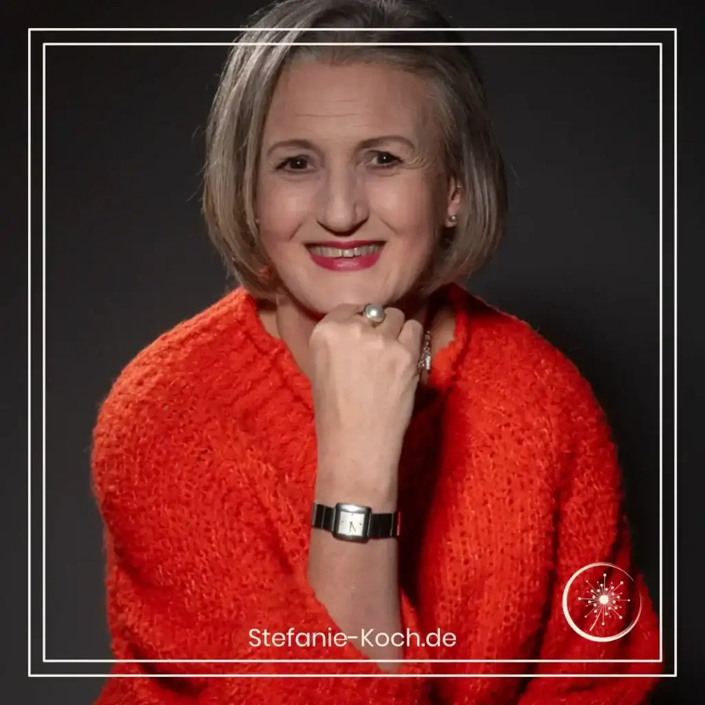 Stefanie Koch im orangefarbenen Pullover vor einer dunklen Wand.