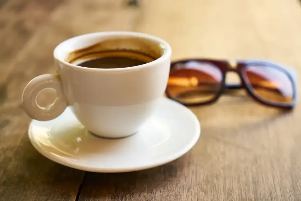 Sommerdepression - weiße Espressotasse steht vor einer Sonnenbrille auf einem Holztisch